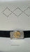 A close-up of a black leather belt with a decorative silver-toned rectangular buckle featuring a gold-toned coin insert, set against a white textured surface with a perforated diamond pattern.