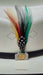 A close-up of a white cowboy hat featuring a black band with a decorative silver-toned coin buckle and a colorful feather accent in red, yellow, black, white, and green.