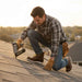 Man working on a roof with a nail gun at sunset