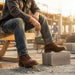 Person wearing brown work boots and jeans sitting on a construction site with 'Built for the Grind' text.