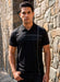 Man wearing a black polo shirt standing against a stone wall