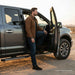 Man standing next to an open door of a silver SUV in a desert setting