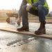 Person working on a construction site wearing brown boots and a high-visibility vest.