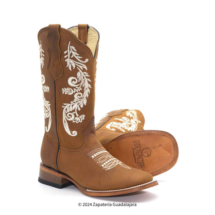 A pair of brown women's leather boots with wide square toes and embossed designs on the sides, featuring a heel and a quilted sole.