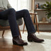 Person wearing brown leather boots and dark jeans sitting on a chair in a home setting.