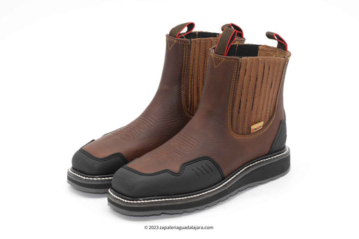 A brown leather work boot with a steel toe cap, displayed alongside its insole and protector. The boot has a lace-up closure and a thick, non-slip sole.