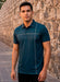Man wearing a teal polo shirt standing against a stone wall.