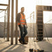 Man in safety vest standing on a construction site with wooden planks and tools around.