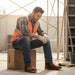 Man in construction attire sitting on a wooden box with tools around him.
