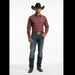 A man modeling a long-sleeve western shirt with a burgundy and brown geometric pattern, paired with blue jeans, a brown cowboy hat, and brown boots against a white studio background.