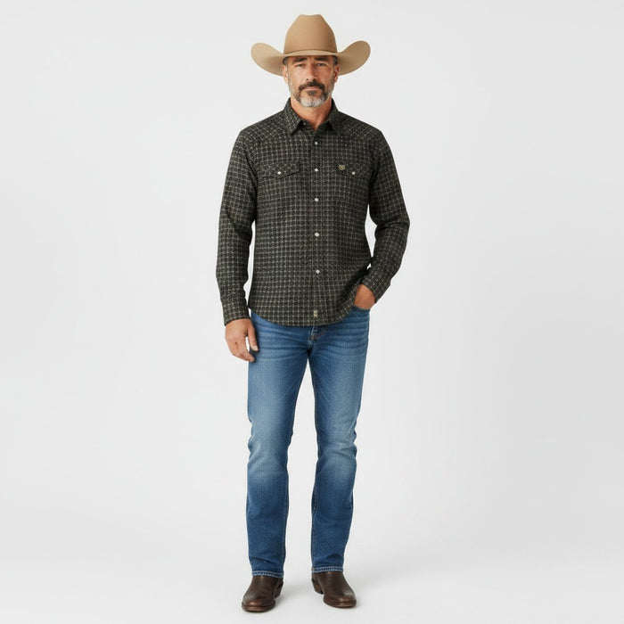 A man modeling a dark green and black checkered western long-sleeve shirt, blue jeans, brown boots, and a tan cowboy hat against a light gray studio background.