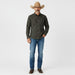 A man modeling a dark green and black checkered western long-sleeve shirt, blue jeans, brown boots, and a tan cowboy hat against a light gray studio background.