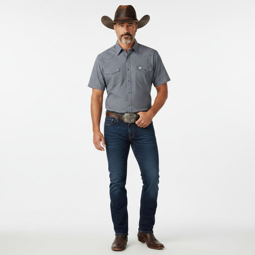 A man modeling a short-sleeve western button-down shirt in heathered blue-gray, paired with dark blue jeans, a brown cowboy hat, and brown leather boots against a plain white studio background.