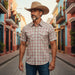 A man wearing a tan cowboy hat and a short-sleeve plaid button-up shirt walks down a colorful street lined with pastel buildings.