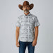 A man wearing a brown cowboy hat, a light gray short-sleeve button-up shirt with a black graphic print, dark blue jeans, and white sneakers, standing against a plain light gray studio background.