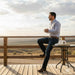 Man sitting on a wooden deck overlooking a scenic landscape with mountains.