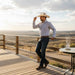 Man in cowboy hat and shirt standing on a wooden deck with a scenic view