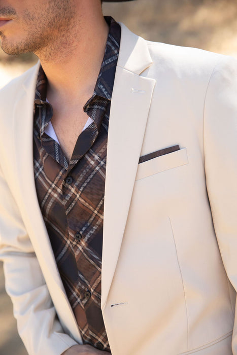 Man wearing a cream blazer over a plaid shirt with a blurred background