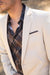 Man wearing a cream blazer over a plaid shirt with a blurred background