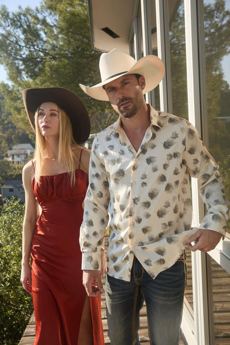 Man and woman in cowboy hats standing outdoors with trees in the background
