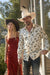 Man and woman in cowboy hats standing outdoors with trees in the background