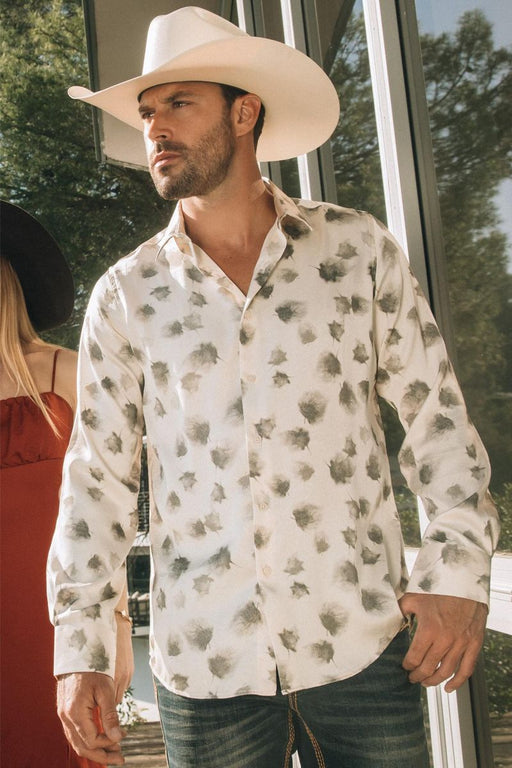 Man wearing a white floral shirt and cowboy hat standing outdoors.