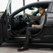 Man sitting inside a car with open door, wearing black shoes with red soles.