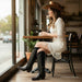 Woman in a white dress and cowboy hat sitting at a cafe table with a cup of coffee.