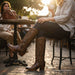 Person wearing brown cowboy boots sitting at a table with a sunset in the background.