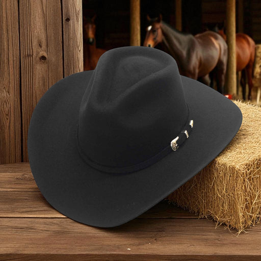 Black cowboy hat on a wooden surface with hay bales and horses in the background