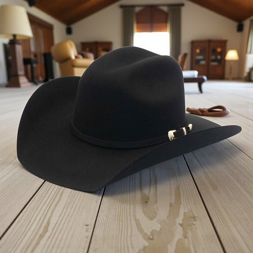 Black cowboy hat with a gold band on a wooden floor in a room with furniture.
