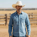 Man wearing a blue denim shirt and cowboy hat in a rural setting