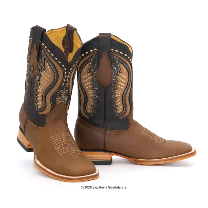 A pair of brown leather cowboy boots with black shaft panels and intricate tan and beige western embroidery, shown on a white background.