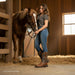 Woman in a barn with a horse, wearing cowboy boots and jeans.