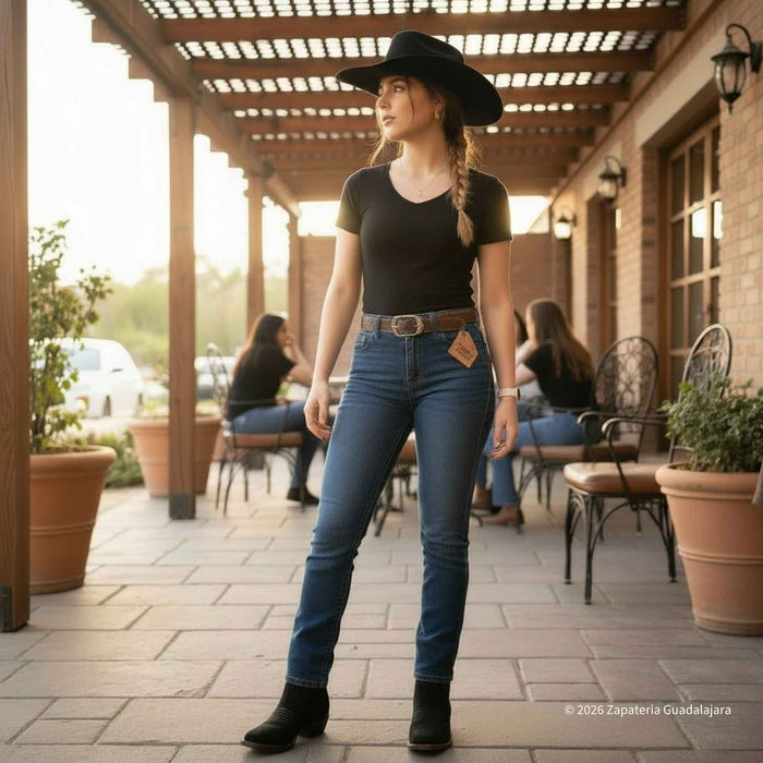 Woman in a cowboy hat and jeans standing on a patio with outdoor furniture in the background.